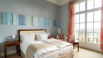 Habitación de hotel con una cama grande, una mesita de noche, una silla y un ventanal con cortinas.