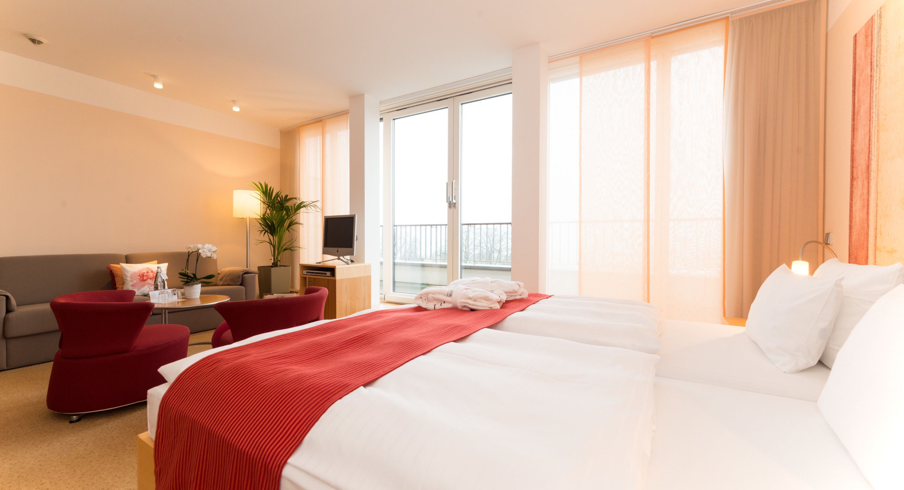 Une chambre d’hôtel avec un grand lit, un bureau avec un ordinateur, une chaise, un canapé et une fenêtre avec des rideaux.