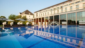 A swimming pool with lounge chairs and umbrellas, a staircase leading to a building, and a large glass facade. - A-ROSA Travemünde (Lübeck)