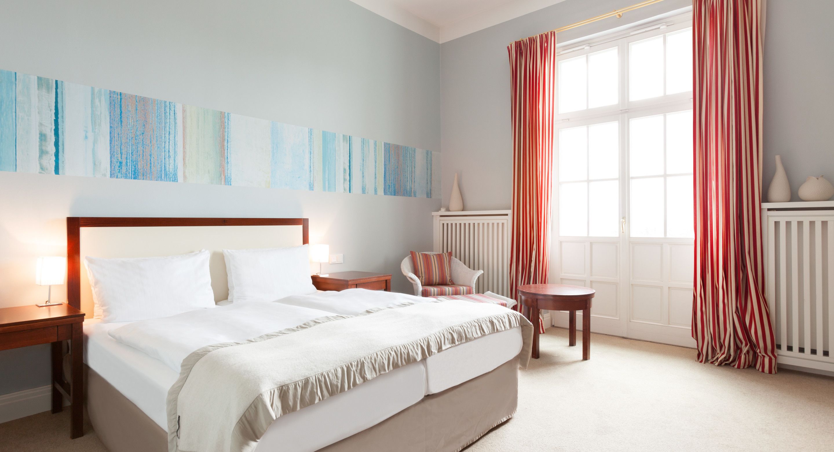 Ein Hotelzimmer mit einem großen Bett, einem Sessel, einem kleinen Tisch und einem Fenster mit Vorhängen.