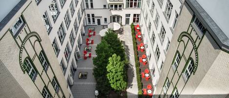 A courtyard with outdoor seating, a central tree, and a building facade with multiple windows and balconies.