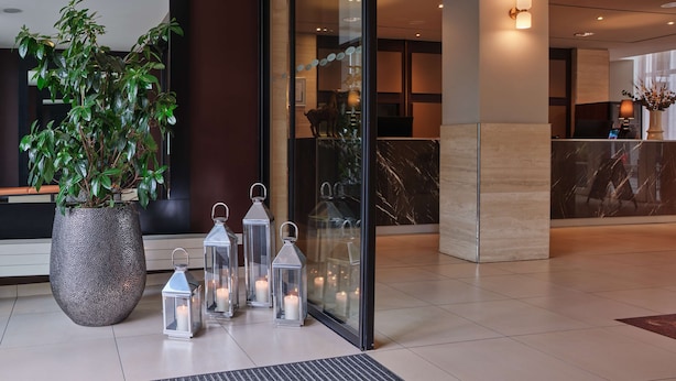 A modern lobby with a large potted plant, several lit lanterns, and a reception desk with a computer. - Adina Apartment Hotel Berlin CheckPoint Charlie (Berlin)