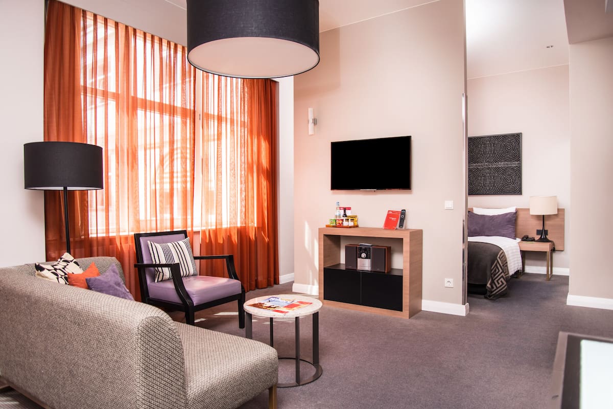 A hotel room with a sofa, armchair, small table, TV, and a bed.
