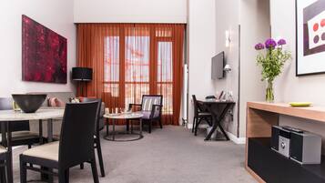 Ein modernes Hotelzimmer mit Essbereich, einem an der Wand befestigten Fernseher und einem großen Fenster mit Vorhängen.