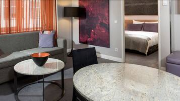 Ein modernes Hotelzimmer mit grauem Sofa, einem runden Tisch und einem Bett mit Kopfteil.