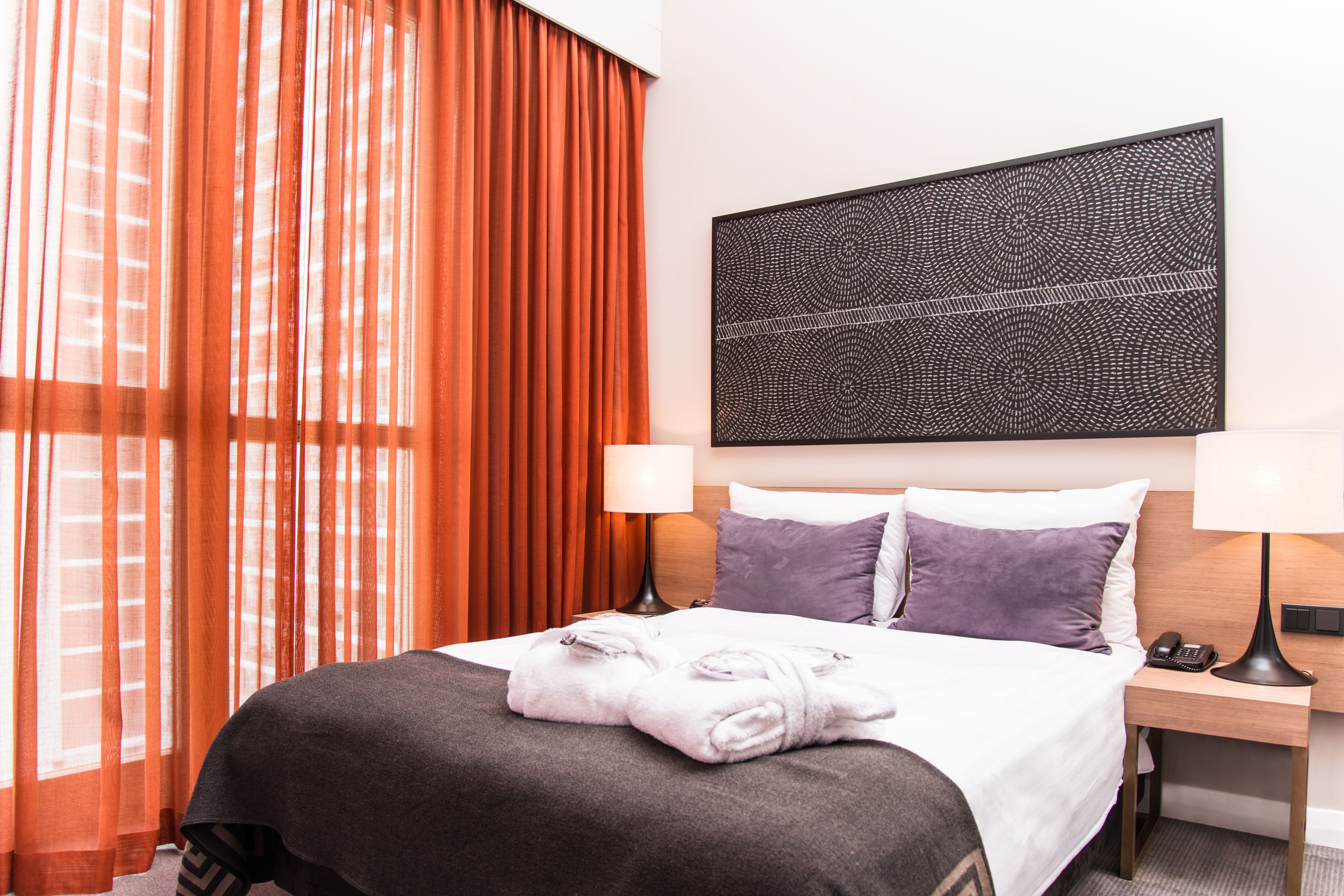 Ein Hotelzimmer mit einem Bett, zwei Nachttischlampen, einem Kopfteil und einem großen, abstrakten Kunstwerk darüber.