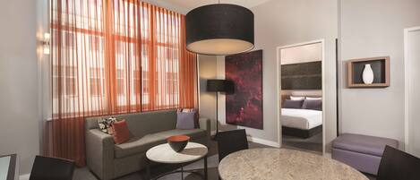 A modern hotel room with a sofa, a round table, a bed, and a large window with curtains.