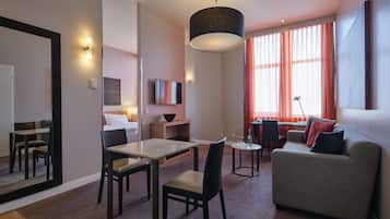 Ein modernes Hotelzimmer mit Essbereich, einer Sitzecke, einem Fernseher und einem großen Fenster mit Vorhängen.