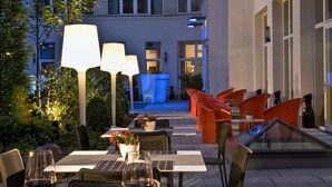 An outdoor dining area with tables, chairs, and ambient lighting. - Adina Apartment Hotel Berlin CheckPoint Charlie (Berlin)