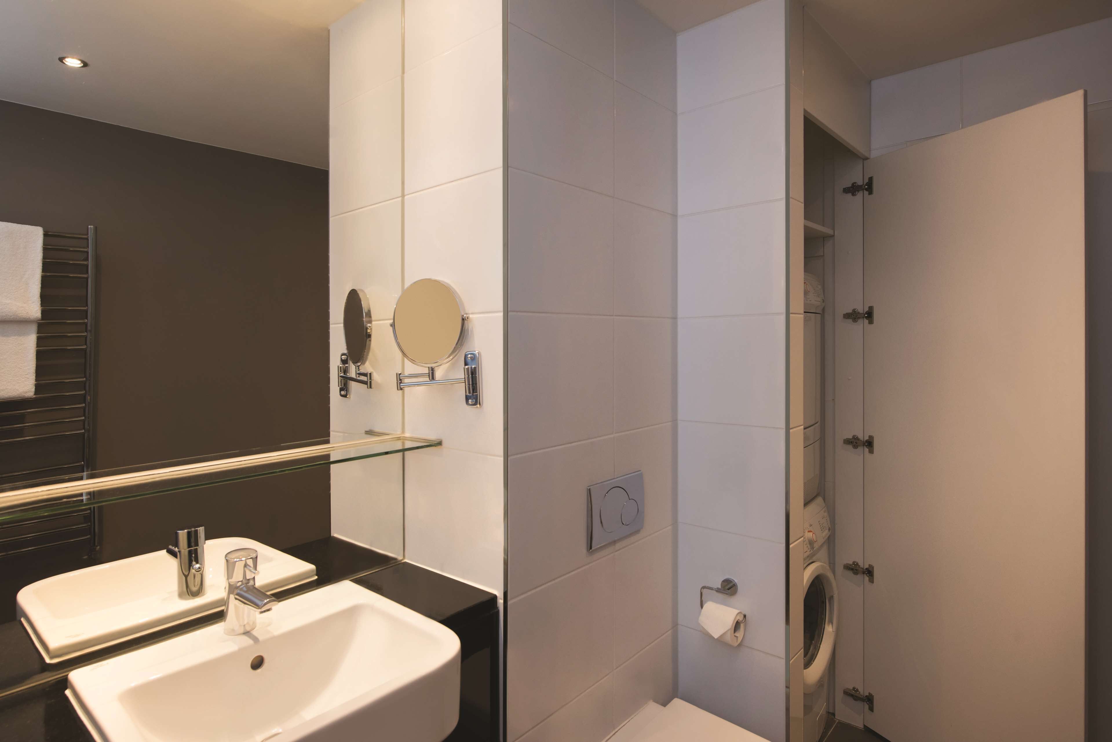 A modern bathroom with a double sink, a glass shower enclosure, and a toilet.