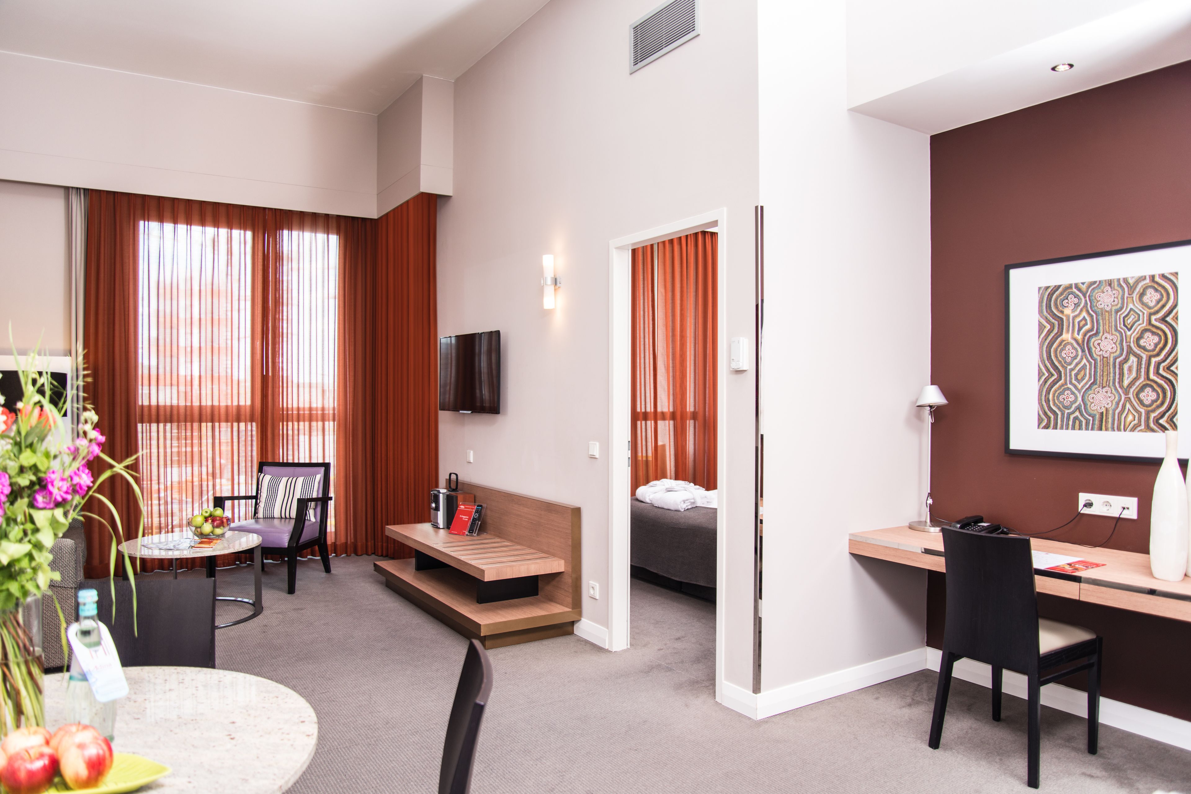 Una habitación de hotel moderna con cama, escritorio, silla y zona de comedor con mesa y sillas.