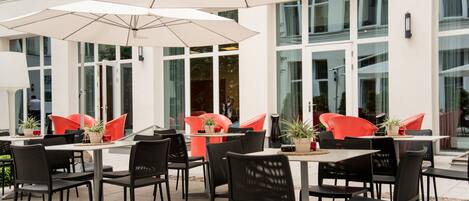 An outdoor seating area with tables and chairs, umbrellas, and potted plants.