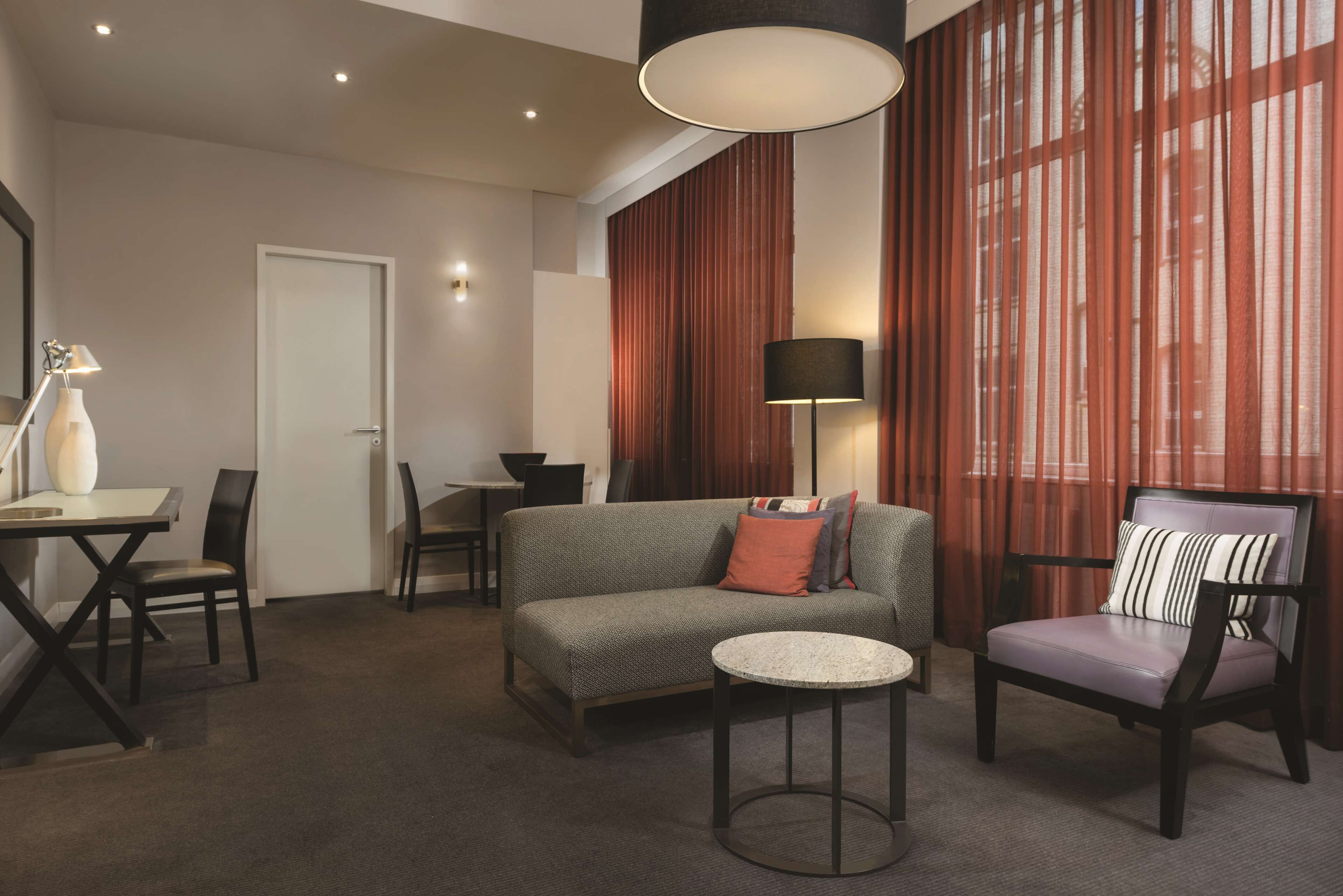 Une chambre d’hôtel moderne équipée d’un canapé, d’un fauteuil, d’une table ronde et d’un coin repas avec des chaises.