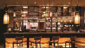 A bar area with multiple shelves of bottles and glasses, bar stools, and a warm ambient light. - Adina Apartment Hotel Berlin CheckPoint Charlie (Berlin)