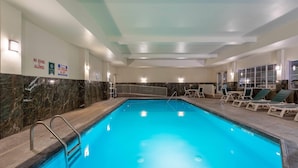 Una piscina interior con zona cristalina, sillas de descanso e iluminación empotrada en el techo.