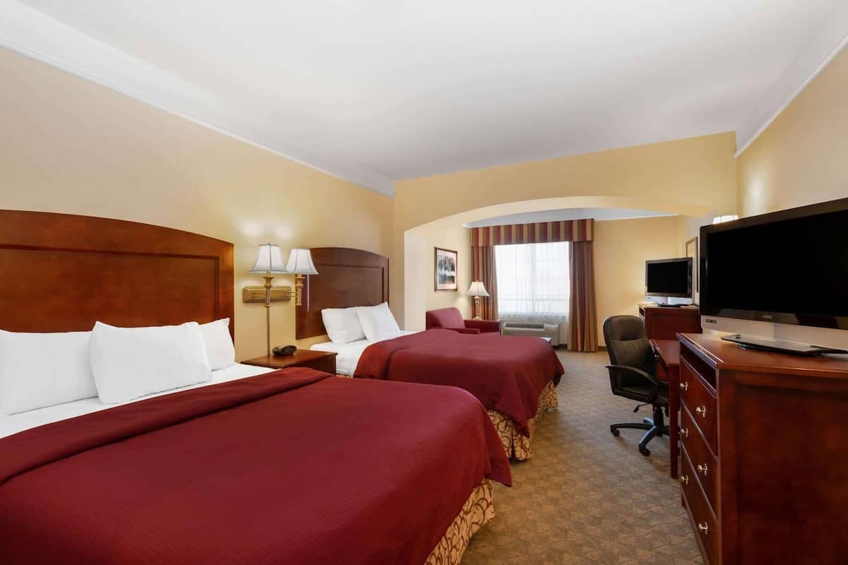 A hotel room with two beds, a television, a desk, and a chair.