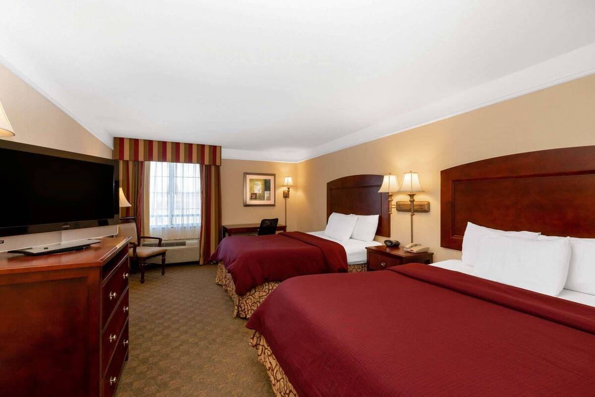 A hotel room with two beds, a TV, a desk, and a chair.