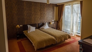 Une chambre d’hôtel avec un grand lit, une tête de lit, une table de chevet avec une lampe et une fenêtre avec des rideaux.