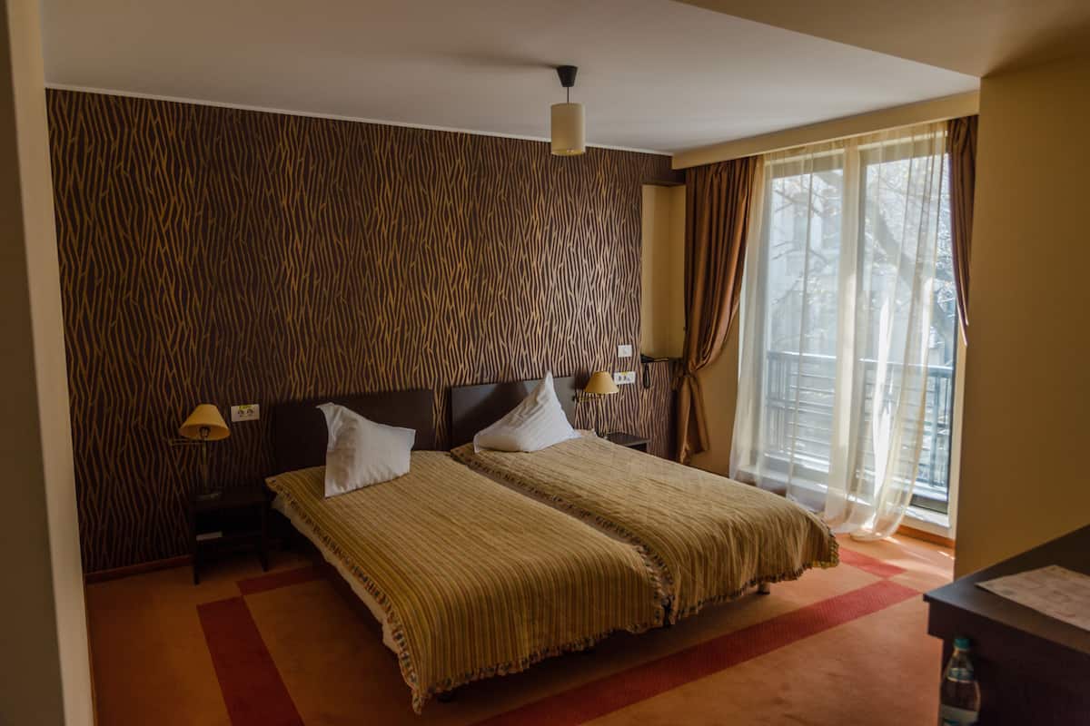 A hotel room with a large bed, a headboard, a nightstand with a lamp, and a window with curtains.