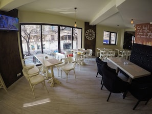Un restaurant avec des tables et des chaises blanches, de grandes fenêtres et une horloge au mur.