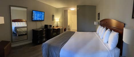 A hotel room with a large bed, a television mounted on the wall, a desk with a lamp, and a dresser.