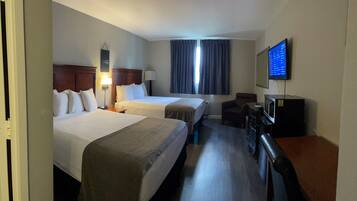 Habitación de hotel con dos camas, un escritorio, un televisor y una ventana con cortinas.