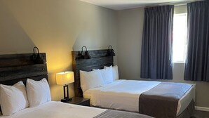 Une chambre d’hôtel avec deux lits, une table de chevet avec une lampe, une fenêtre avec des rideaux et une tête de lit en bois.