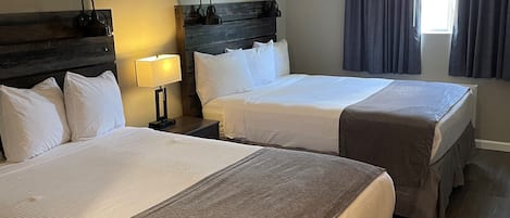 Una habitación de hotel con dos camas, una mesita de noche con lámpara, una ventana con cortinas y un cabecero de madera.