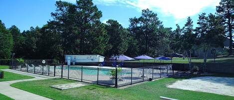 A fenced outdoor area with a pool, picnic tables, and umbrellas.