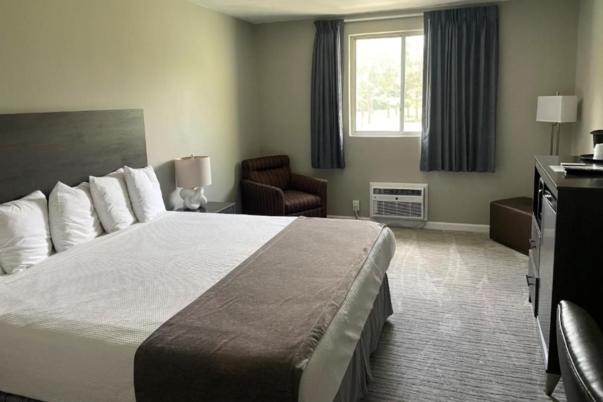 A hotel room with a large bed, a chair, a desk, and a window with curtains.