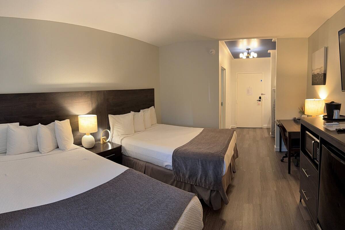 Una habitación de hotel con dos camas, un escritorio, una silla y una pequeña kitchenette.