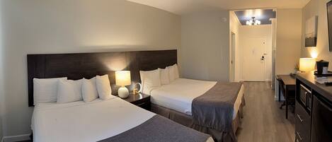 Een hotelkamer met twee bedden, een bureau, een stoel en een kleine kitchenette.