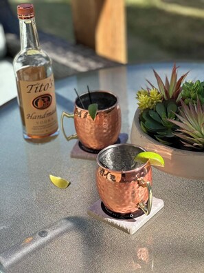 A table with a bottle of Tito's Handmade Vodka, two copper mugs with straws, a lime wedge, and a potted succulent plant.
