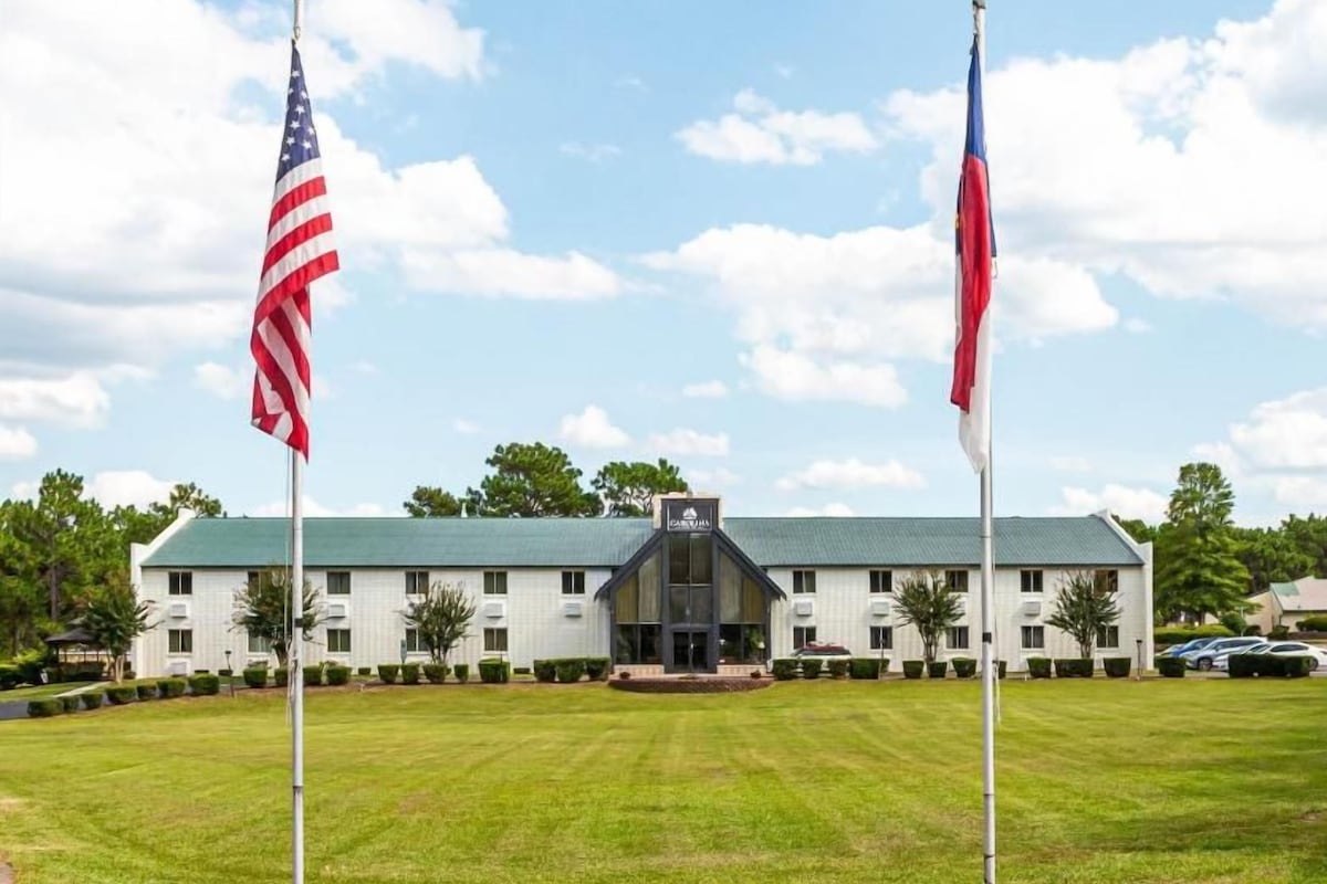 A building with a green roof, two flags, and a well-maintained lawn.