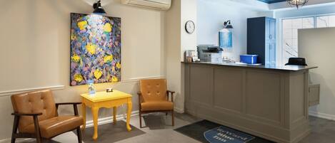 A reception area with a desk, chairs, a clock, and a painting on the wall.