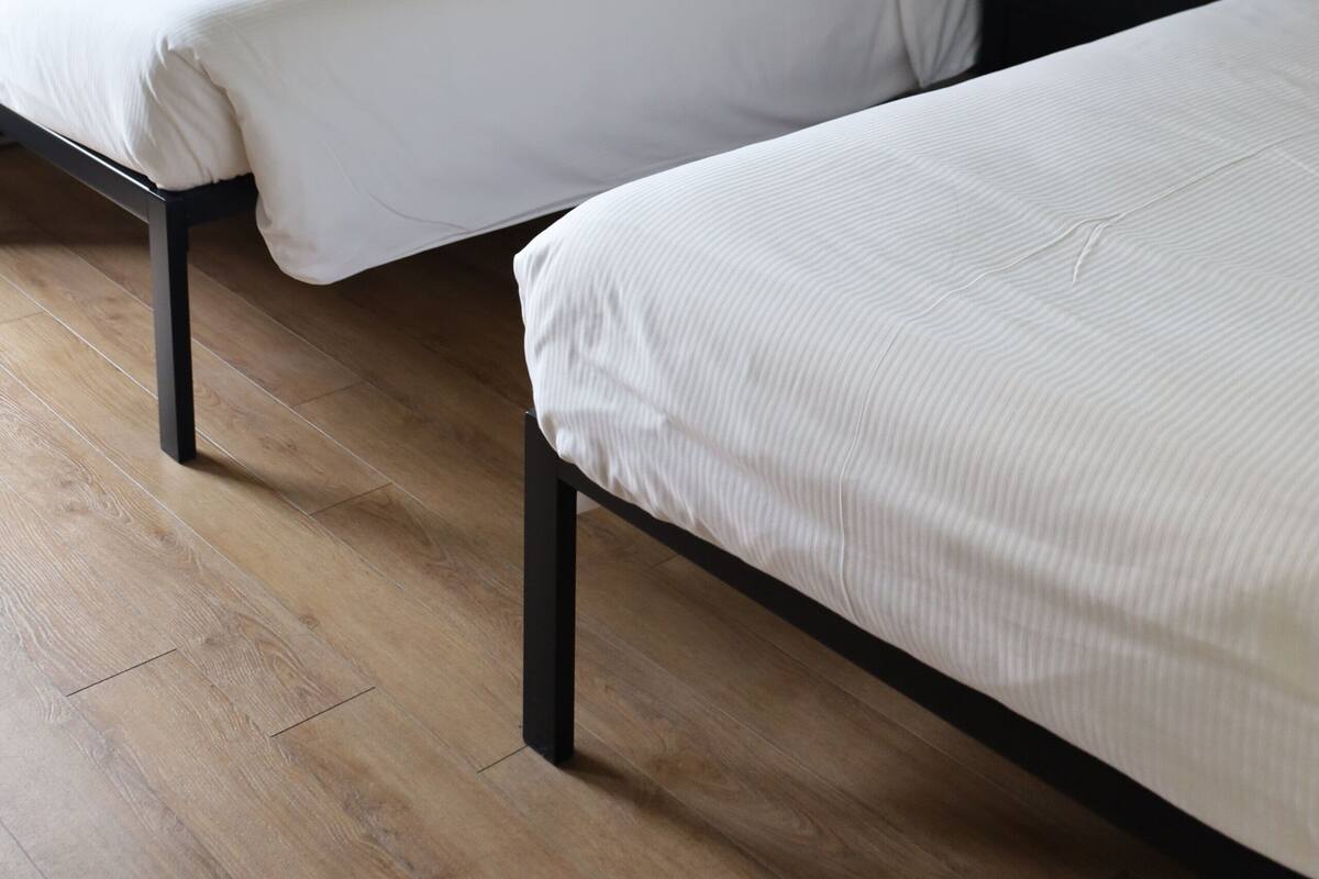 A hotel room with two single beds, a bedside table with a lamp, and a window with curtains.