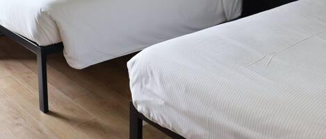 Habitación de hotel con dos camas individuales, una mesita de noche con lámpara y ventana con cortinas.