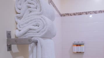 Un baño con un perchero blanco que sostiene varias toallas, una zona de ducha y un pequeño estante con artículos de aseo.