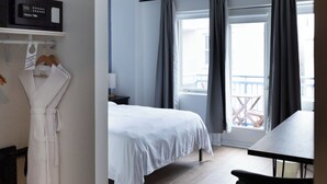 Une chambre d’hôtel comprenant un lit, un bureau, une chaise, un peignoir suspendu à un porte-manteau et un balcon avec des rideaux.