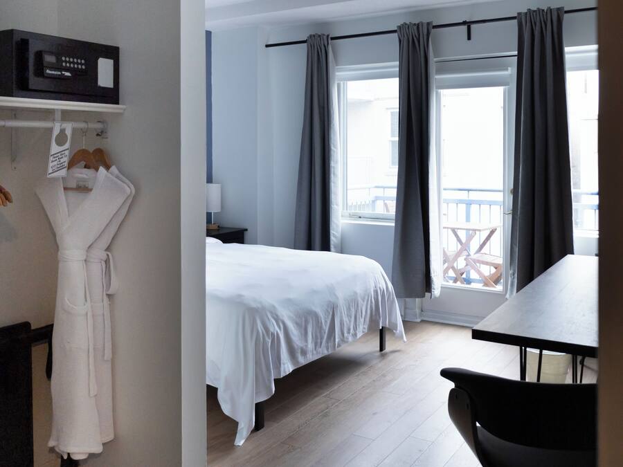 Een hotelkamer met een bed, een bureau, een stoel, een badjas hangend aan een rek en een balkon met gordijnen.