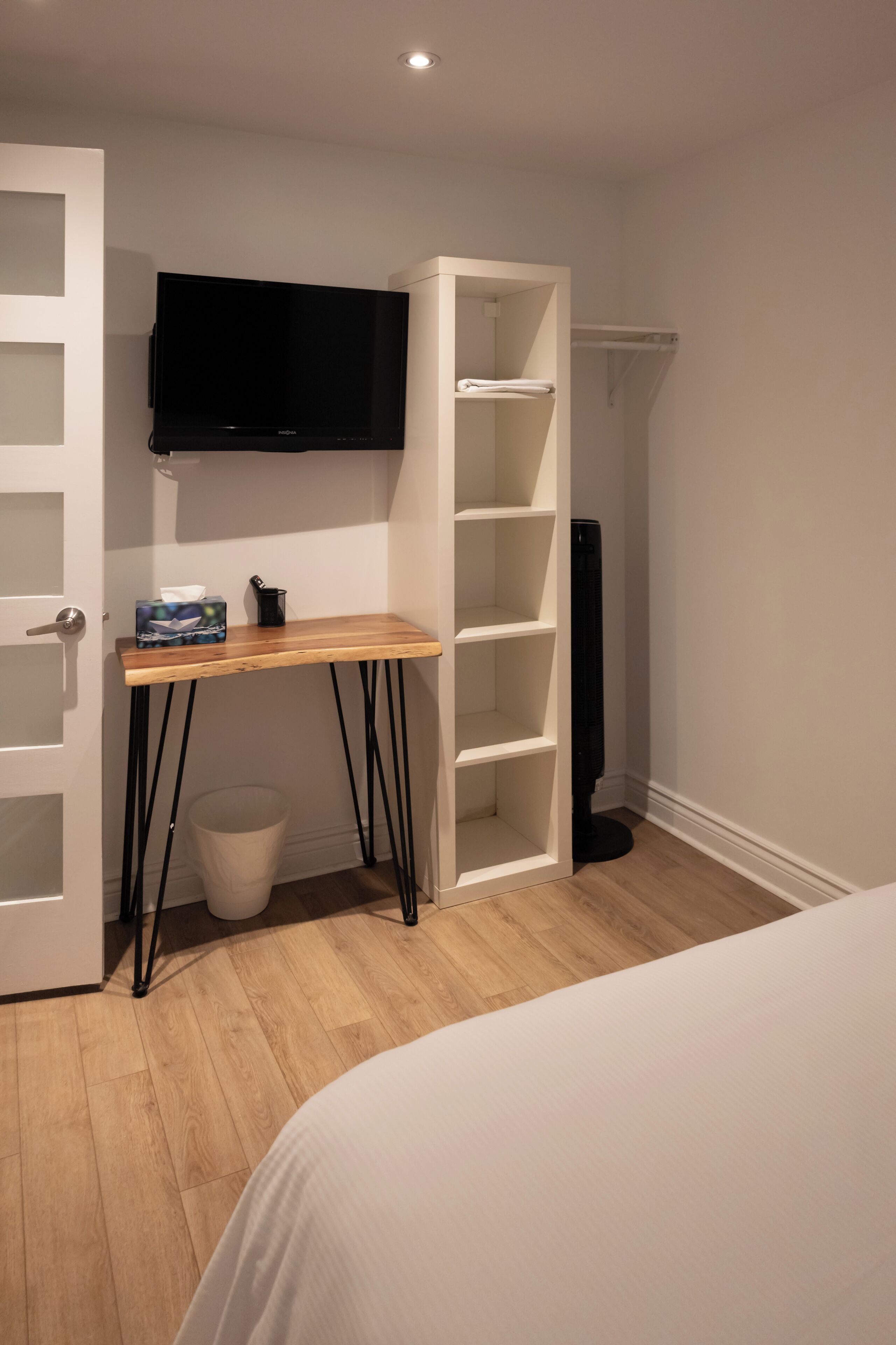 Un dormitorio con cama, un escritorio de madera, televisión, armario y un cubo de basura.