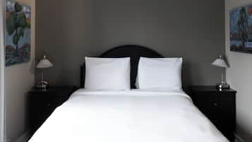 Una cama bien tendida con sábanas blancas, un cabecero oscuro y dos mesitas de noche con lámparas.
