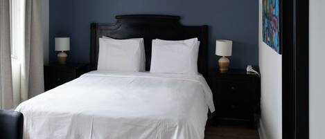 A hotel room with a large bed, a bedside table with a lamp, a chair, and a wall with a colorful painting.