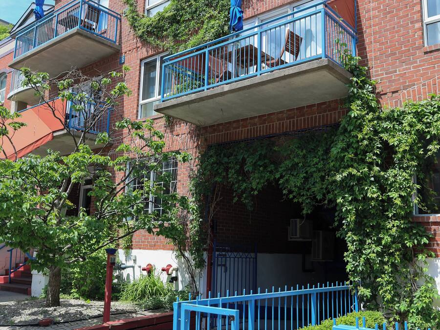 A multi-story brick building with balconies, a gated entrance, and a clear sky.