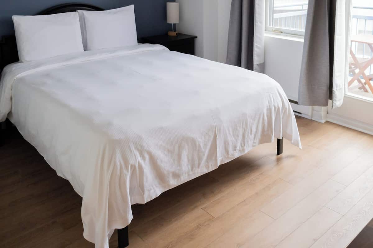 A bedroom with a bed, a nightstand, a window with curtains, and a view of buildings outside.