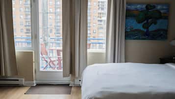 A hotel room with a large bed, a view of the city through a glass door, and a painting on the wall.