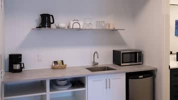 Una cocina compacta con armarios blancos, microondas, cafetera y lavavajillas.