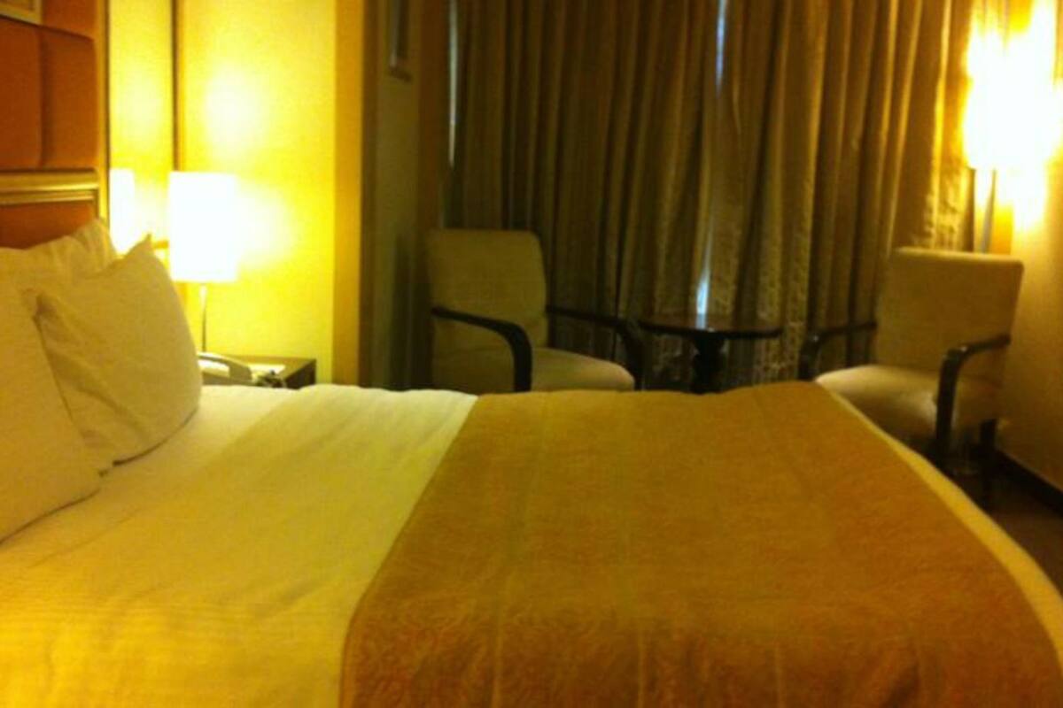 A hotel room with a large bed, two chairs, a small table, and two lamps.