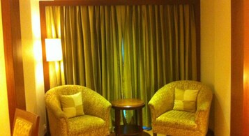 Quarto com duas poltronas, uma mesa redonda pequena, uma luminária e um fundo de cortina.