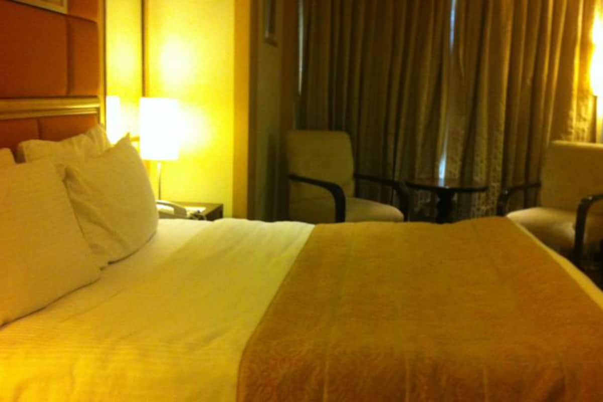 A hotel room with a large bed, two chairs, a small table, and a lamp.